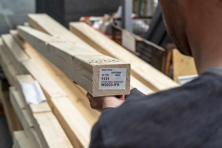 STREIF Produktion Mitarbeiter hält Holzbauteil mit Etikett vor gestapelten Holzbalken in Werkhalle