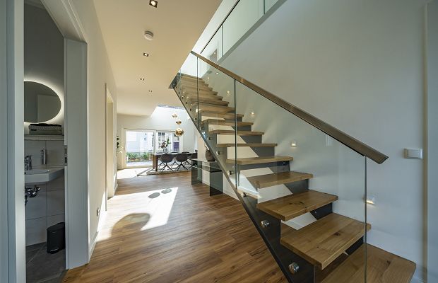STREIF Innenraum Flur mit offener Treppe aus Holz und Glasgeländer, heller Wohnbereich im Hintergrund