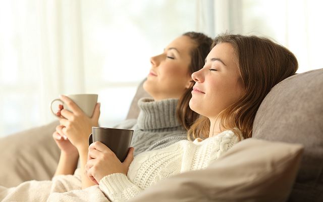 Innenraum Wohnzimmer zwei Personen entspannen auf Sofa mit Tassen, sitzen im Tageslicht am Fenster