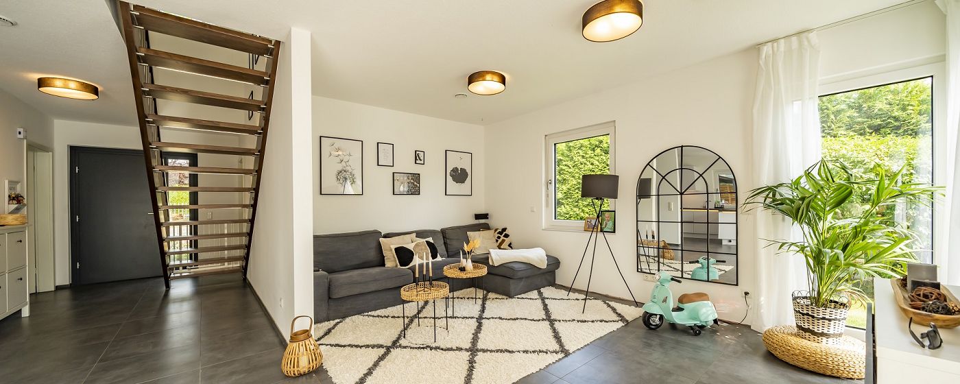 STREIF Innenraum Wohnzimmer mit Sofa, Teppich, offener Treppe und großen Fenstern in heller Gestaltung