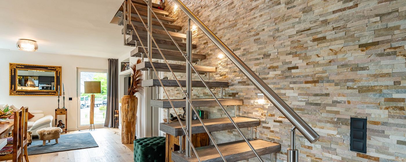 STREIF Innenraum Wohnbereich mit offener Treppe aus Holz und Metall, Steinwand und moderner Einrichtung