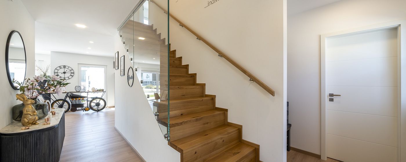 STREIF Innenraum Flur mit Holztreppe, Glasgeländer, Sideboard und hellem Eingangsbereich