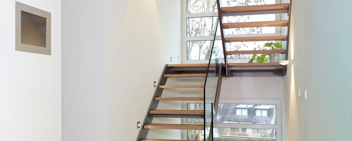 STREIF Innenraum Treppe mit offenen Holzstufen, Glasgeländer und großen Fensterflächen im Treppenhaus