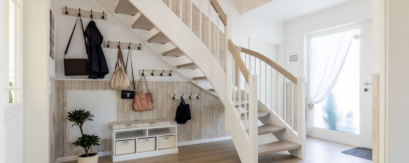 STREIF Innenraum Flur mit halbgewendelter Holztreppe, Garderobe, Sitzbank und hellem Eingangsbereich