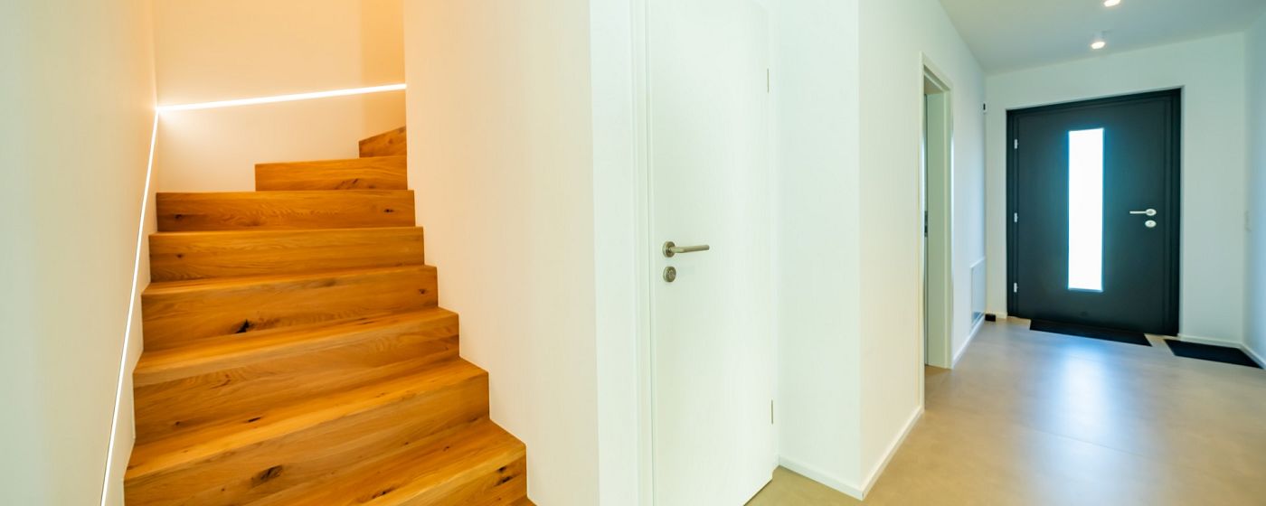 STREIF Innenraum Flur mit halbgewendelter Holztreppe, weißer Wand und moderner Eingangstür