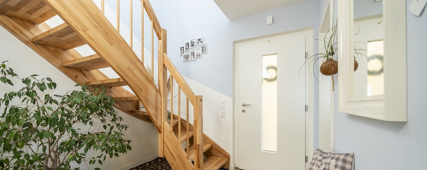 STREIF Innenraum Flur mit halbgewendelter Holztreppe, Geländer und Pflanzen neben Hauseingangstür