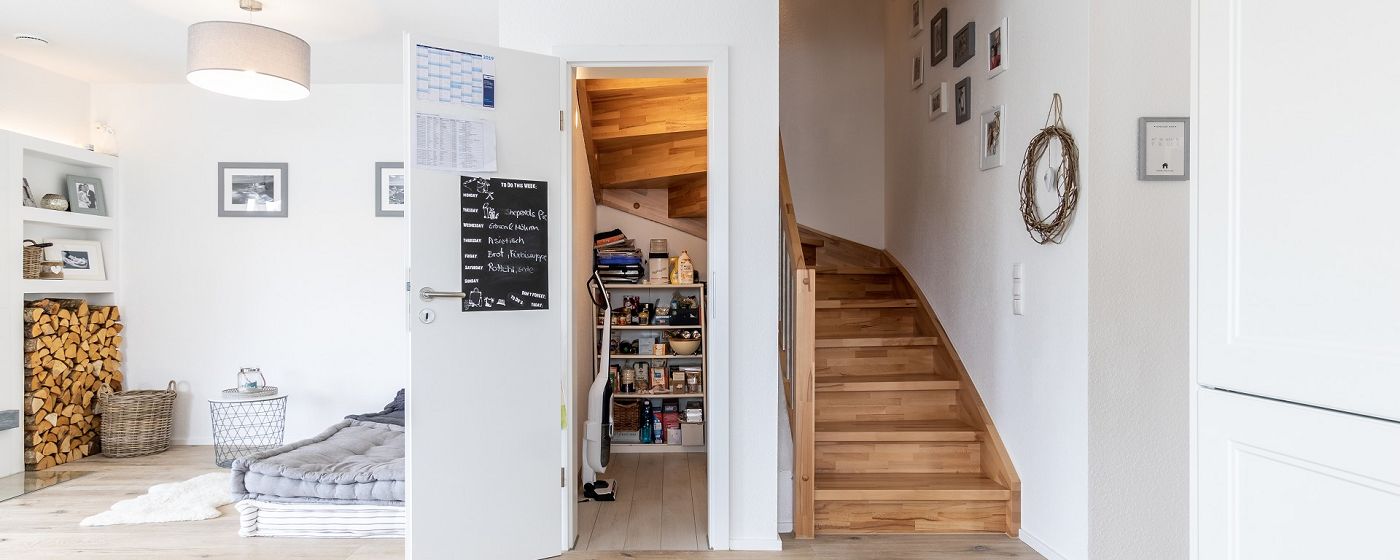 STREIF Innenraum mit halbgewendelter Holztreppe, Zugang zum Abstellraum und Wohnbereich im Hintergrund