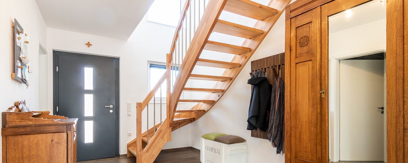 STREIF Innenraum Flur mit halbgewendelter Holztreppe, Garderobe und dunkler Hauseingangstür