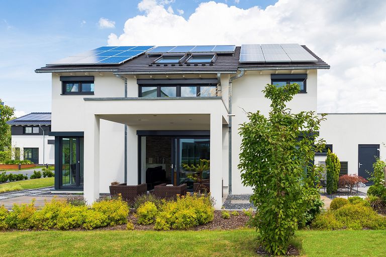 Fertighaus Stadtvilla zweigeschossig mit Satteldach und Solaranlage, weiße Putzfassade, große bodentiefe Fenster, überdachte Terrasse, Garten