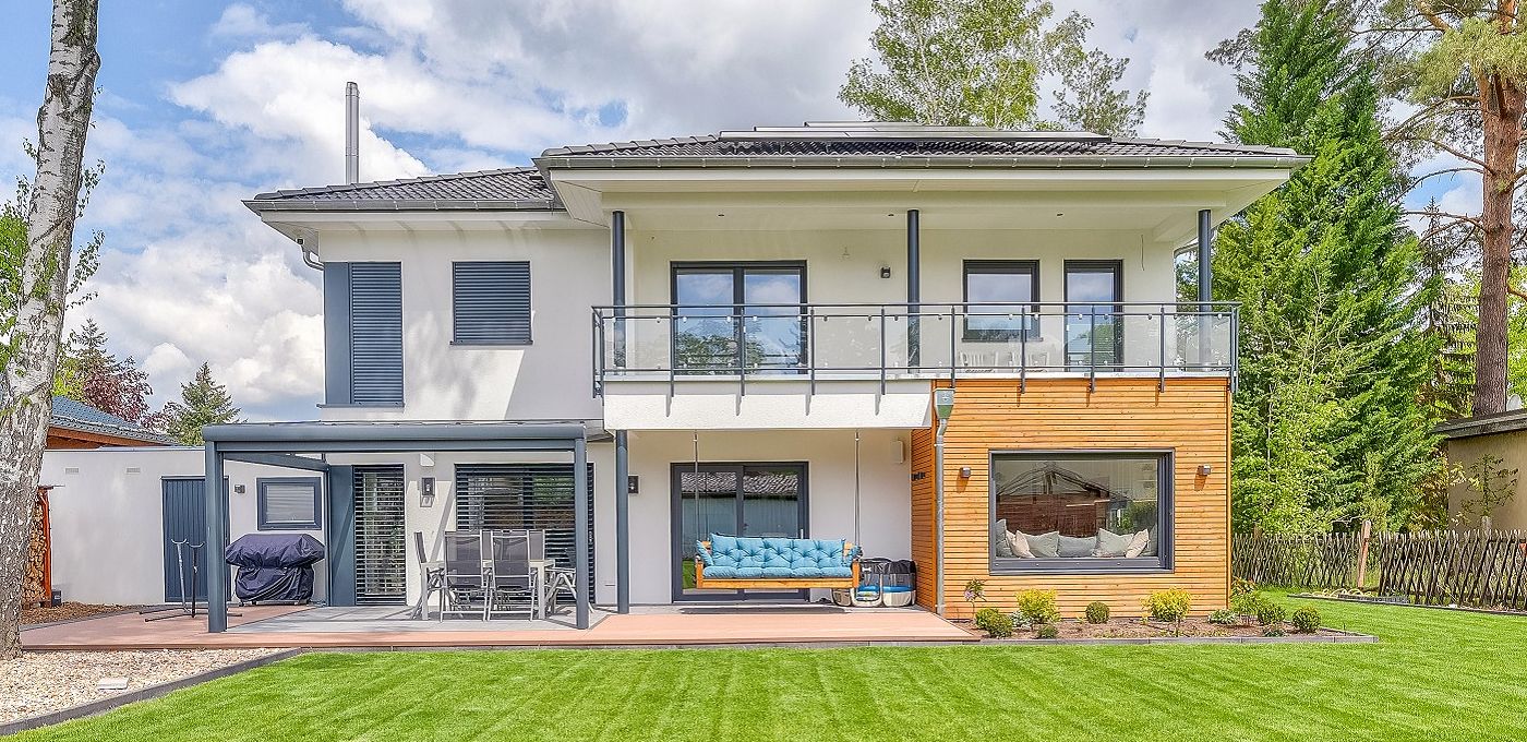 Fertighaus Stadtvilla zweigeschossig mit Walmdach, weißer Putz-Holzfassade, Balkon, Terrasse und Garten