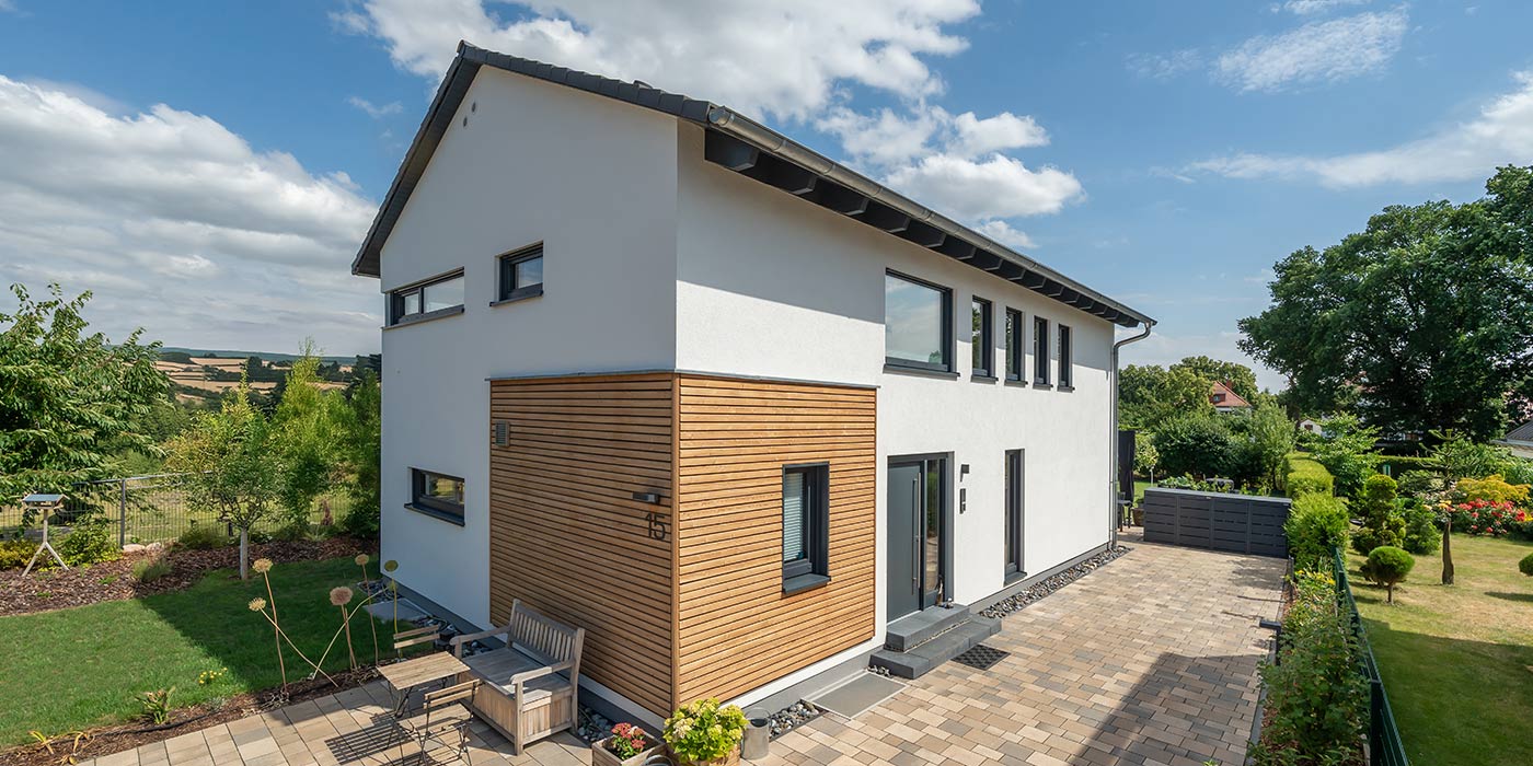 Fertighaus Einfamilienhaus zweigeschossig mit Satteldach, weißer Putz-Holzfassade, Einfahrt und Garten