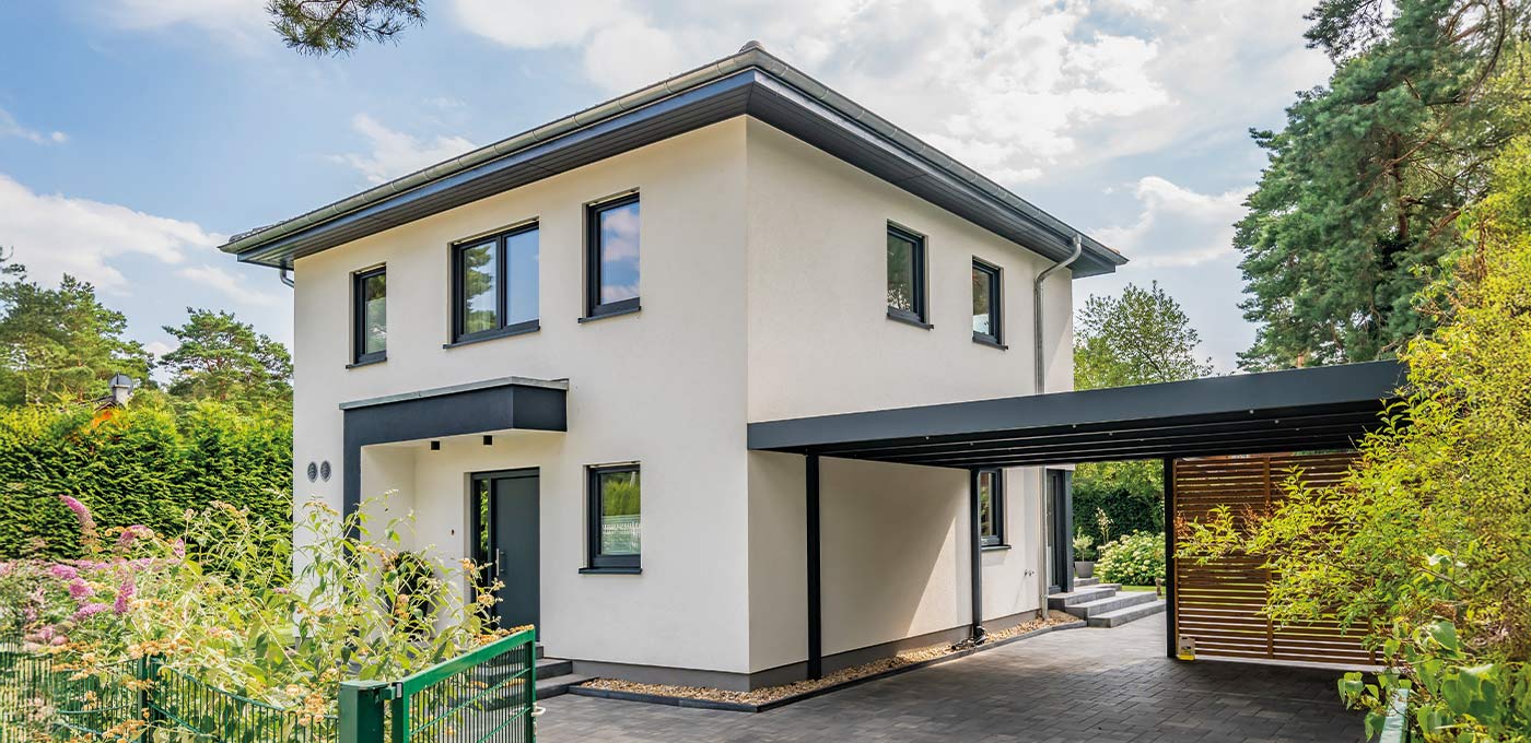 Fertighaus Stadtvilla zweigeschossig mit Walmdach, heller Putzfassade, Carport und Einfahrt