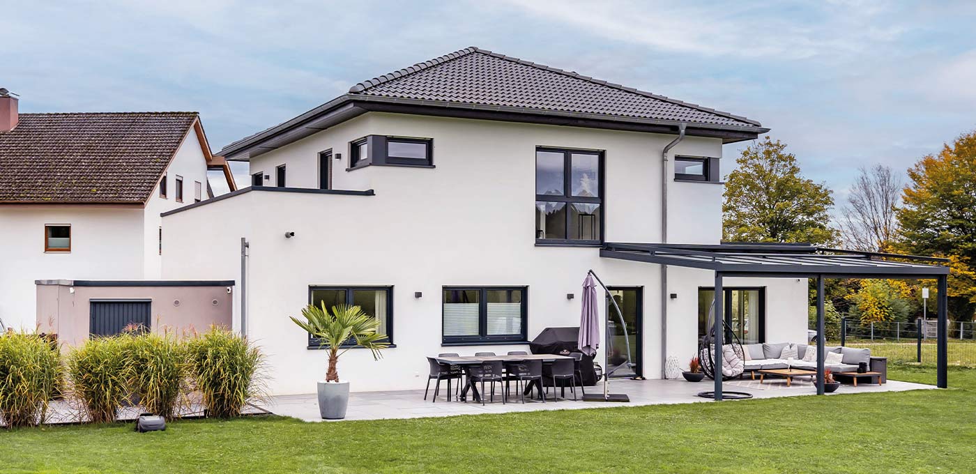 Fertighaus Stadtvilla zweigeschossig mit Walmdach, heller Putzfassade, Terrasse, Pergola und Garten