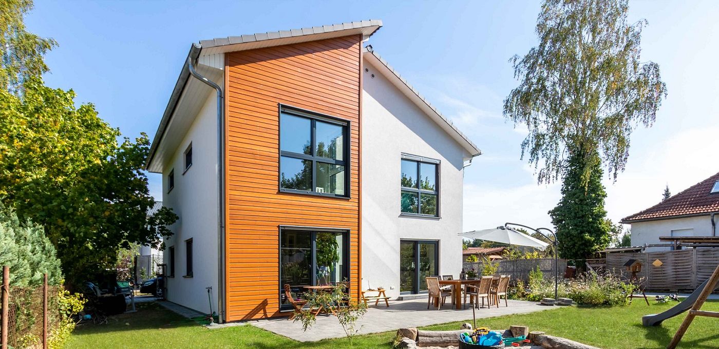 Fertighaus Einfamilienhaus zweigeschossig mit Satteldach, weißer Putzfassade, Holzakzent, Terrasse und Garten