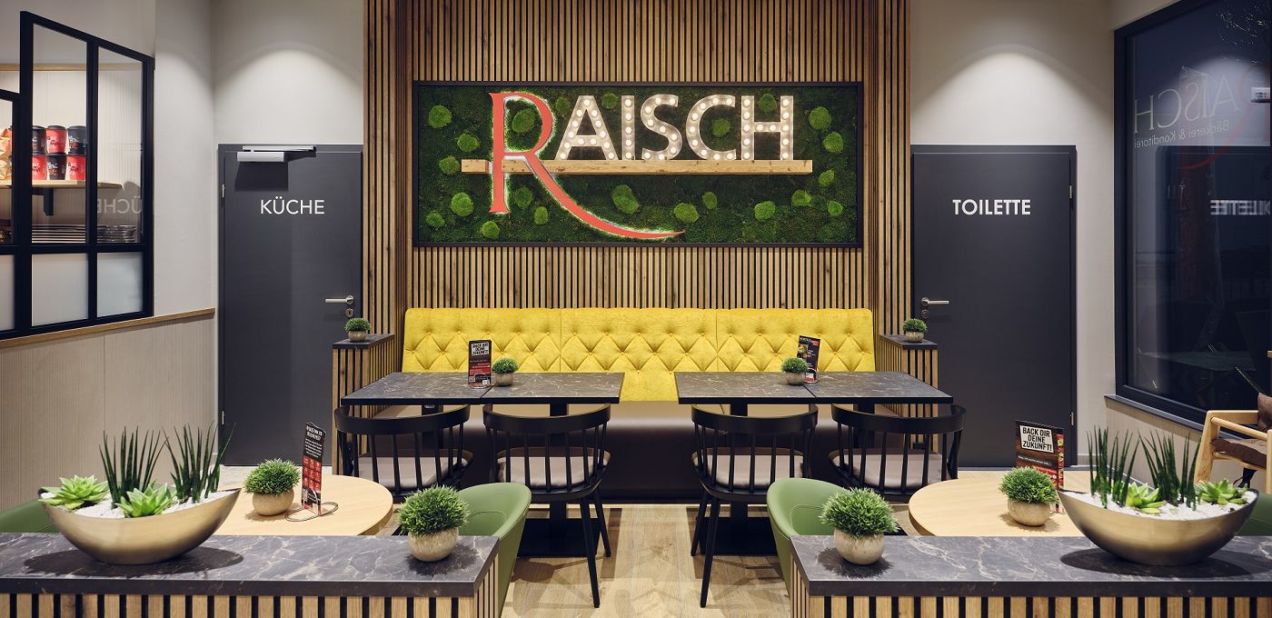 STREIF Innenraum Bakery Cube Sitzbereich mit Polsterbank, Tischen, Wandbegrünung und beleuchtetem Logo