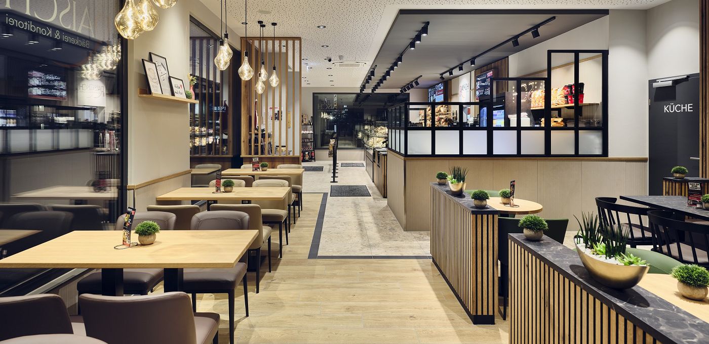 STREIF Innenraum Bakery Cube Sitzbereich mit Tischen, gepolsterten Stühlen, Thekenbereich und moderner Beleuchtung