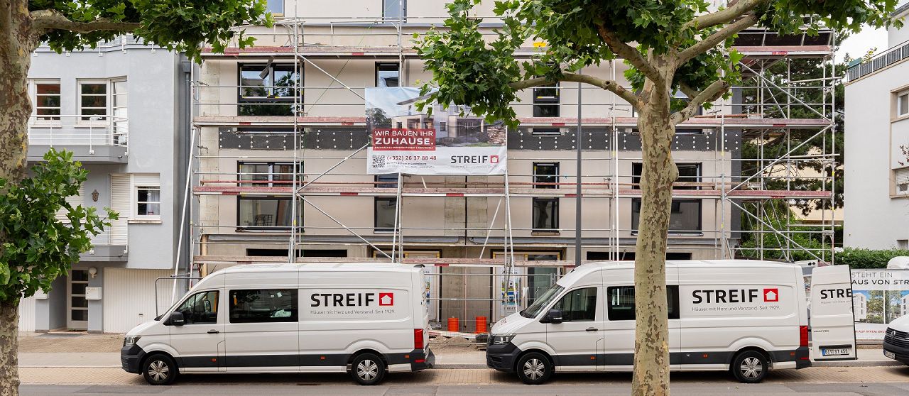 STREIF Baustelle Mehrfamilienhaus im Bau mit Gerüst, Firmenfahrzeugen und Banner an der Fassade