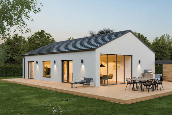 Fertighaus Bungalow mit Satteldach, großer Holzterrasse und beleuchteter Außenansicht bei Abenddämmerung