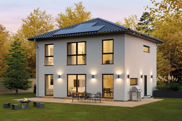 Fertighaus Stadtvilla mit Walmdach, beleuchteter Terrasse und Garten in Außenansicht bei Abendlicht