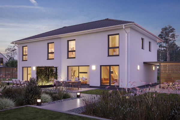Fertighaus Stadtvilla mit Walmdach, beleuchteter Terrasse und Garten in Außenansicht bei Dämmerung